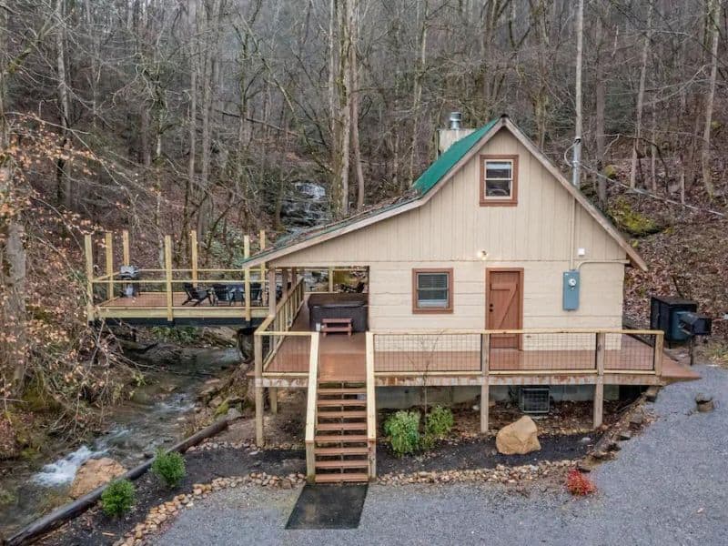 Exterior view of cabin with a deck built over a stream with wooded area in the background