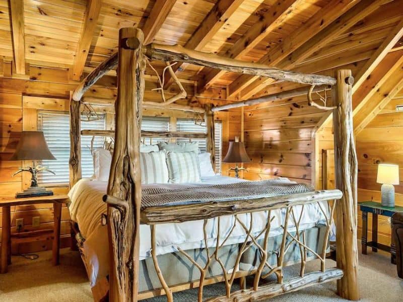 Master bedroom of Pigeon Forge cabin, featuring a natural wood branch constructed bed, plush neutral accents, and floor to ceiling wood paneling.