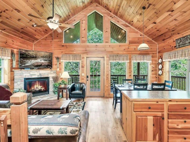 Living area of Pigeon Forge rental cabin, with fireplace, rustic wooden interior, and forest views.