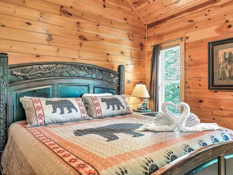 Cabin style Bedroom, with bear print quilt, wood paneling, and forest views.
