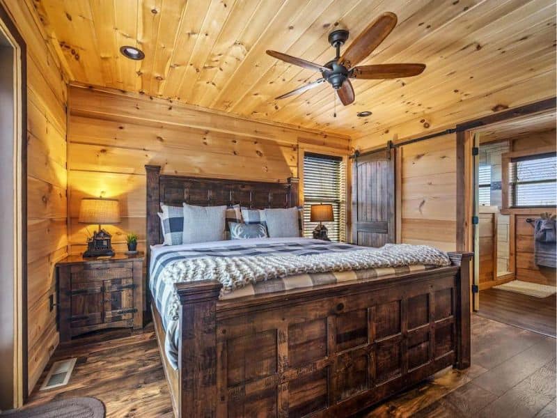 Bedroom with rustic styling, wooden paneling throughout, and barn doors to the attached bathroom.