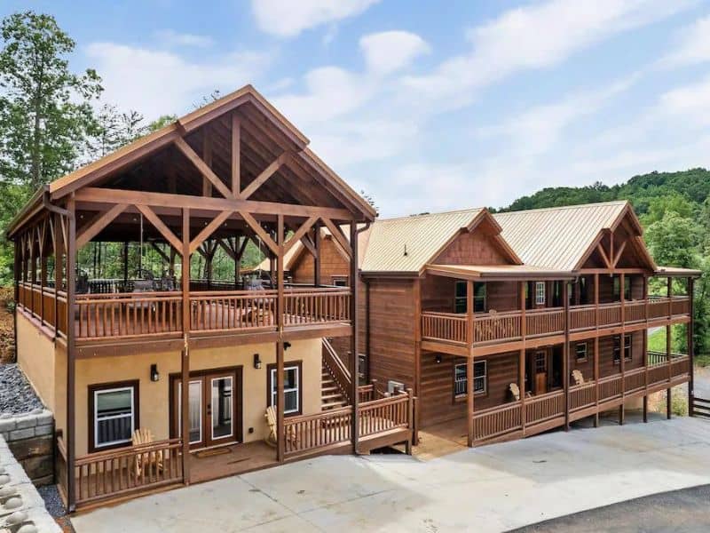 Exterior of Pigeon Forge vacation home. Two log cabins sit side by side with exposed angled beams, one with an open deck on the top floor, surrounded by forest.