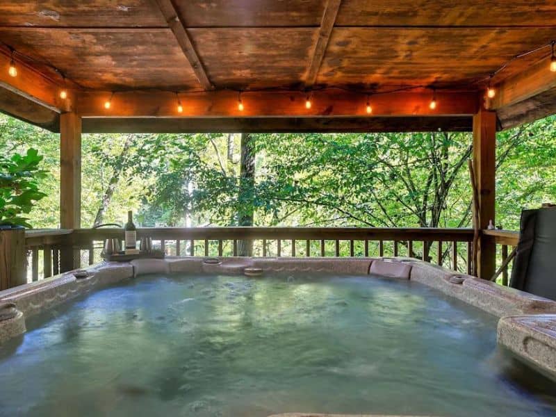 Balcony Jacuzzi with accent lights looking out into a forest view of Pigeon Forge rental cabin.