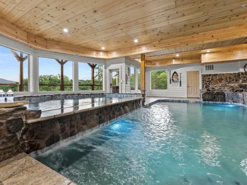 Two leveled indoor pool of Pigeon Forge cabin rental, with rustic detailing and views of forested mountains outside.