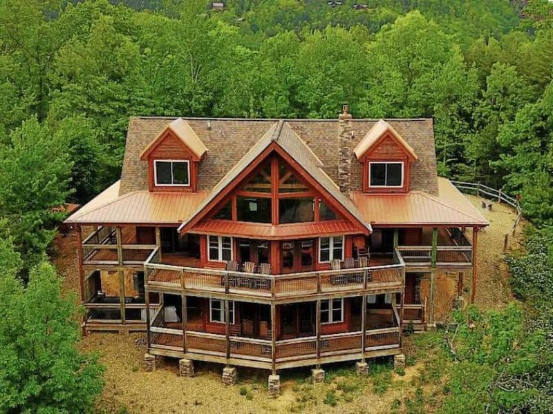 Exterior of Pigeon Forge cabin rental, with dual level wrap around porches, wood constructed, and surrounded by green forest.