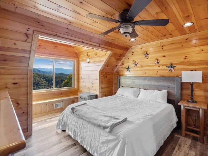 Bedroom with wood paneling and rustic accents, and views of forest and mountains of Pigeon Forge Cabin rental.
