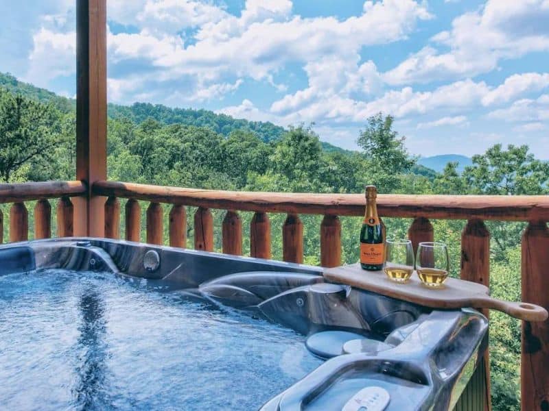 Outdoor Jacuzzi with wine poured for two, looking out from the balcony at forested mountains at Pigeon forge vacation rental.