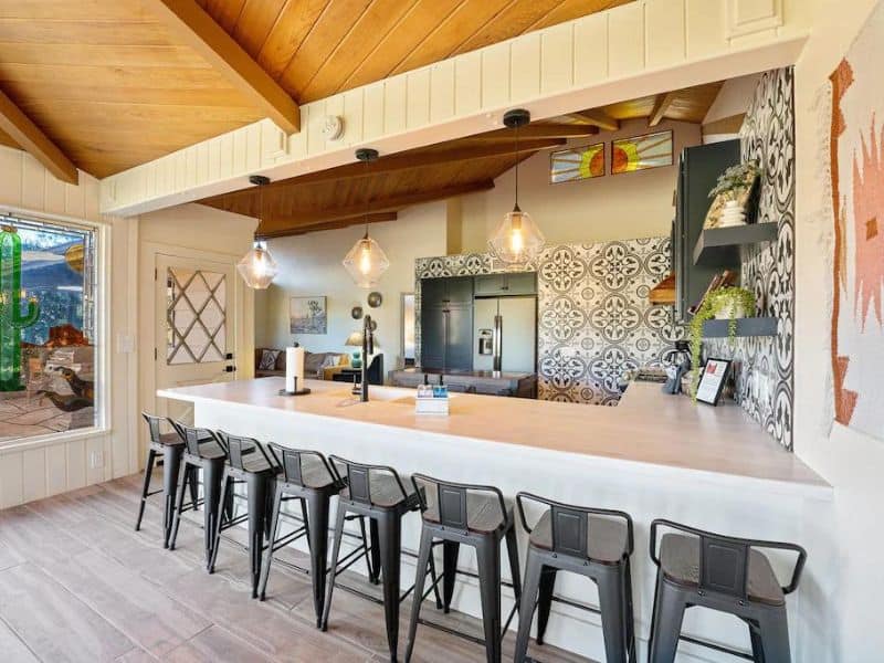 Open plan kitchen with lots of black barstools for seating and a mosaic tile backsplash