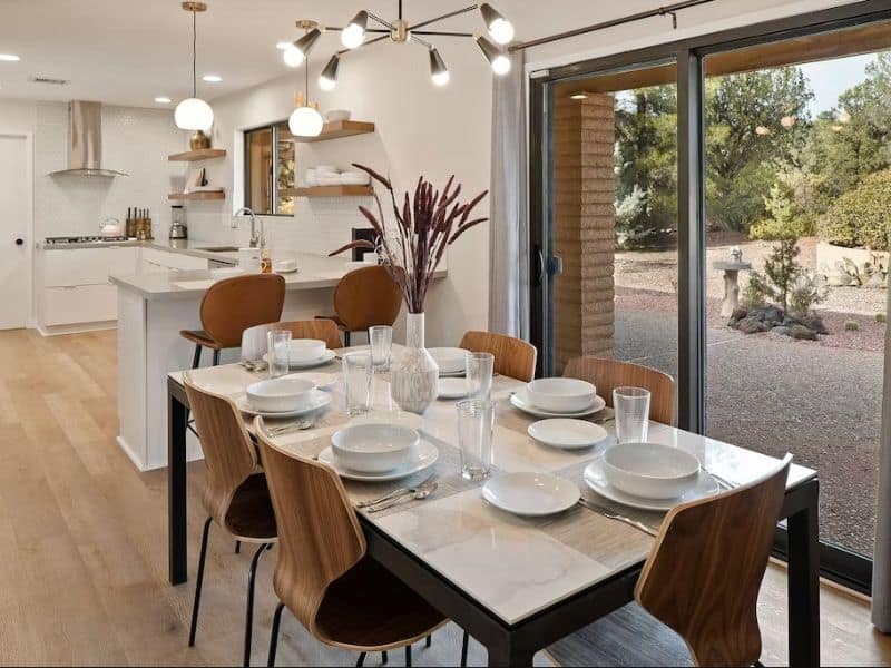 Contemporary dining table with modern lighting and white kitchen in the background
