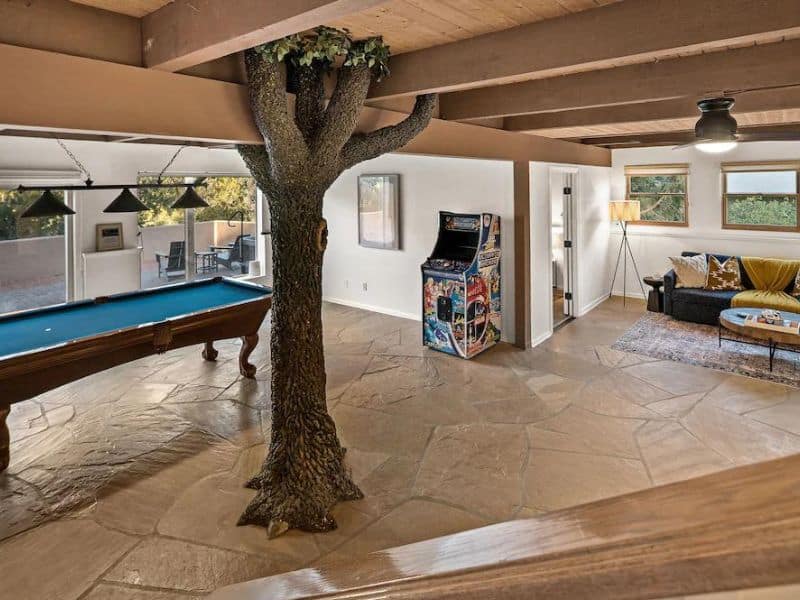 Basement entertainment area in Sedona vacation home, with pool table, arcade games, and couch, with a natural tree growing through the middle of it.