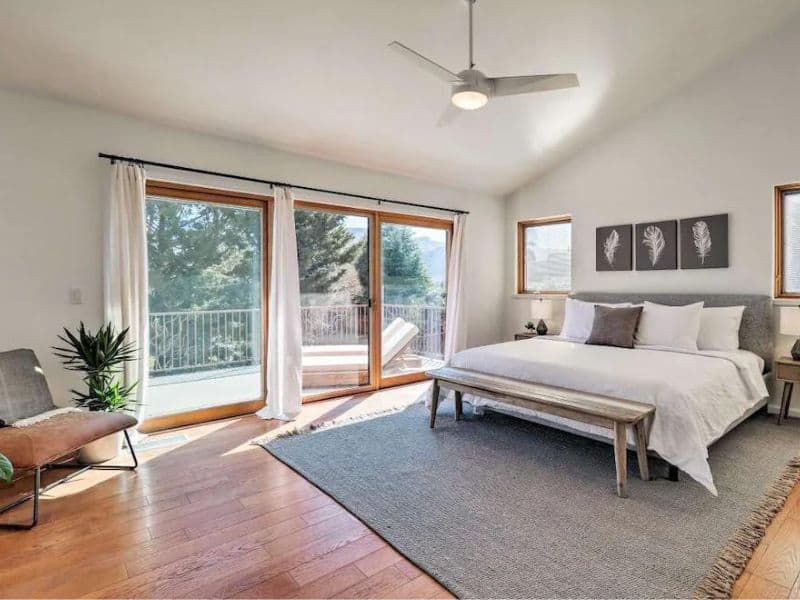 Spacious king bedroom with white linens and curtains, lots of natural light, and a large grey floor rug