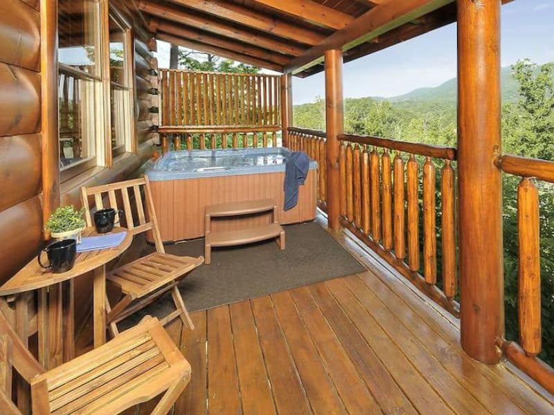Rear porch of Pigeon Forge vacation cabin with seating are and jacuzzi tub, views of surrounding forest.