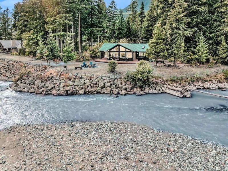 Wide angle shot of cabin with green roof on a river - part of a guide to the best cabins near Mt Rainier