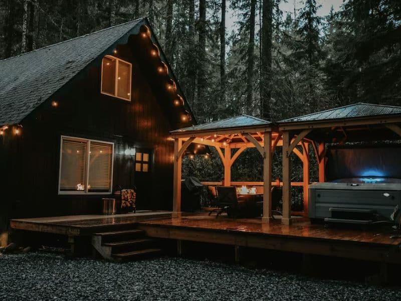 Cabin rental in Ashford WA at dusk with string lights and covered fire pit and hot tub
