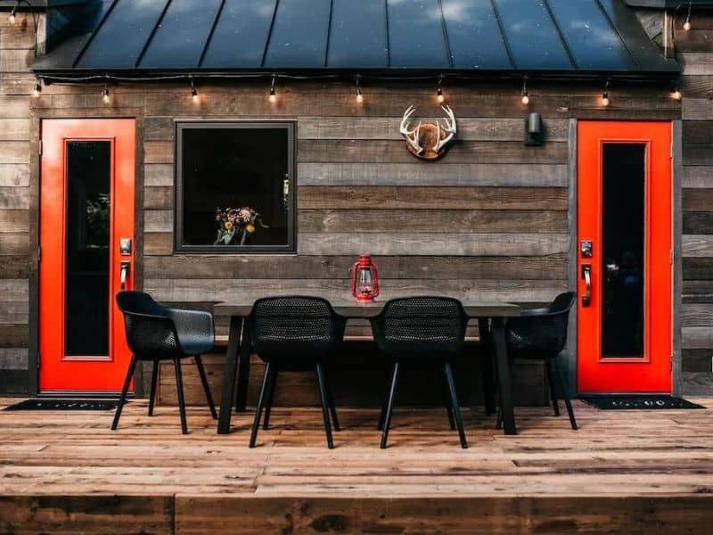 Tiny house wood cabin exterior with deck and outdoor dining table and red doors - part of a guide to the best cabins near Mount Rainier, WA