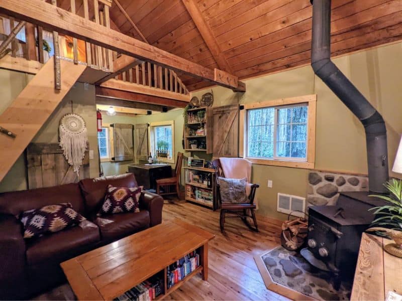 Cozy cabin interior with wood cast-iron fireplace, small seating area and upstairs loft
