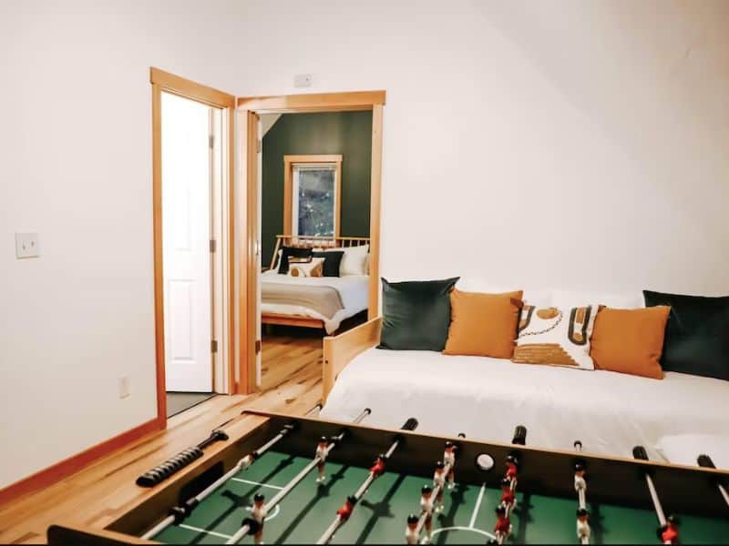 Foosball table with day bed with view into bedroom with green accent wall.