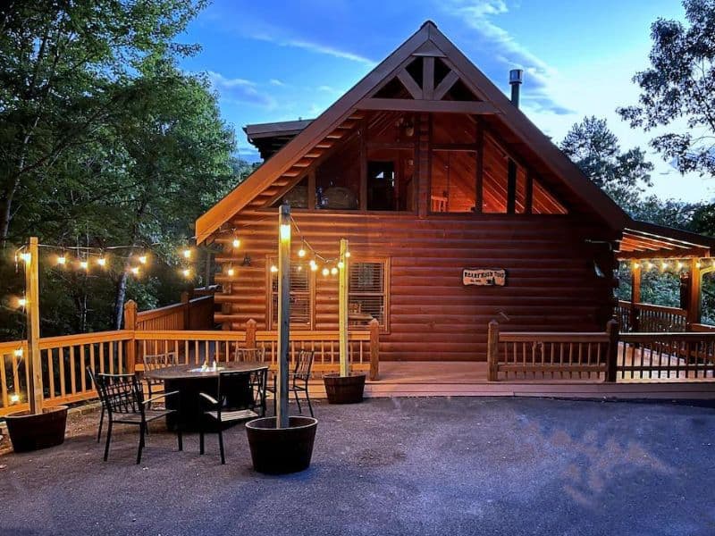 Exterior of log cabin with vaulted ceilings and an outdoor sitting area and fire pit with strung fairy lights - part of a guide to the best pet-friendly cabins in Gatlinburg