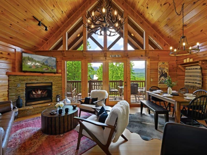 Modern rustic living area in Gatlinburg cabin with vaulted ceilings, large windows, stone fireplace, and area rugs