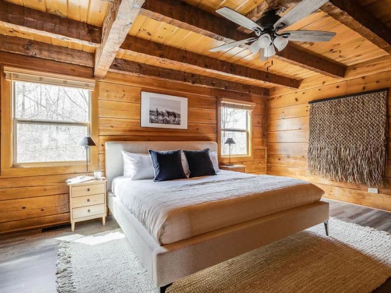 Large master suite in wood cabin with exposed beams and ceiling fan