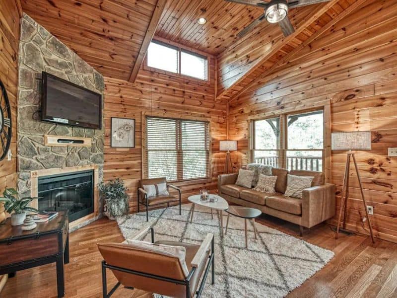Modern rustic living room at dog-friendly cabin in Gatlinburg with leather couches, area rug, fireplace and TV