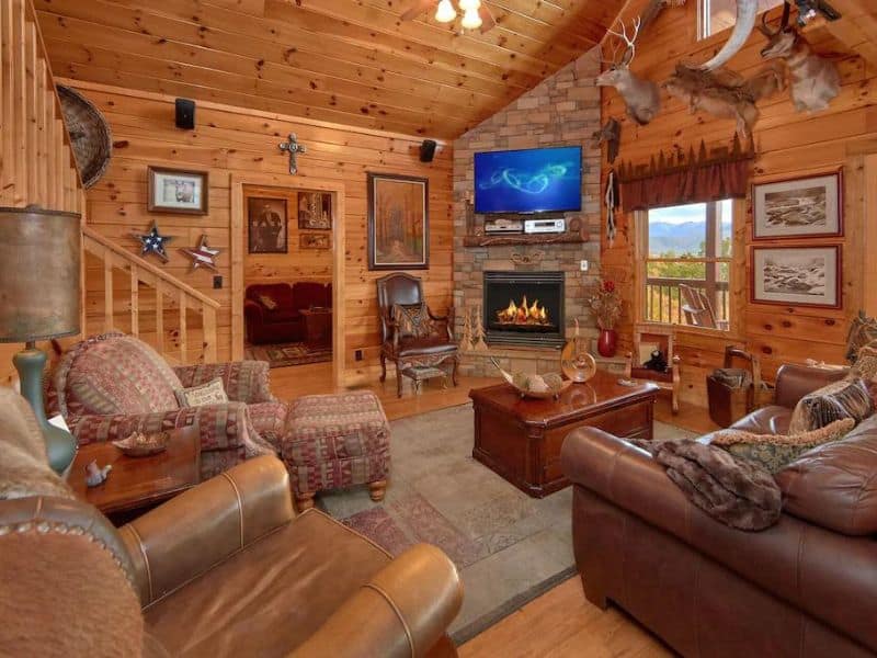 Cozy rustic living area in wood cabin rental with stone fireplace and TV