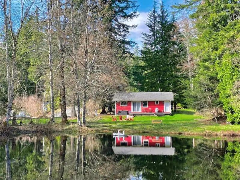 Charming red cabin located on a pond and surrounded by trees - part of a guide to the best Mt Rainier cabins to rent