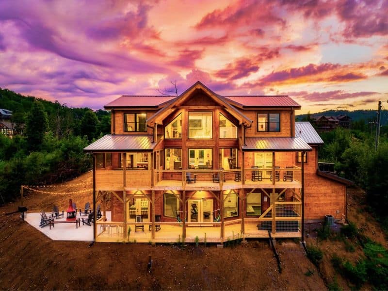 A large multi-level cabin in Gatlinburg lit up at sunset with a pink sky in the background - part of a guide to the best large cabin rentals in Gatlinburg TN