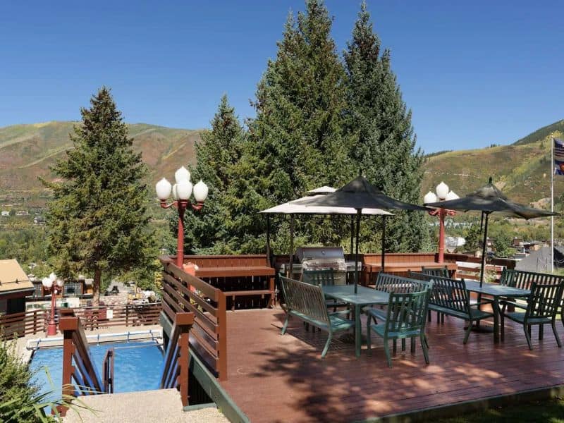 A deck with tables and chairs overlooking a pool and mountains.
