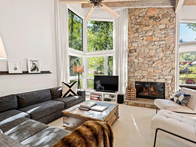 A living room with stone walls and a fireplace at a ski in ski out condo rental in Aspen CO.
