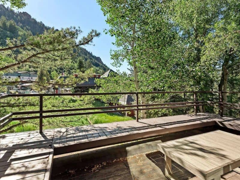 A balcony in Aspen CO overlooking a wooded area with a table and chairs.