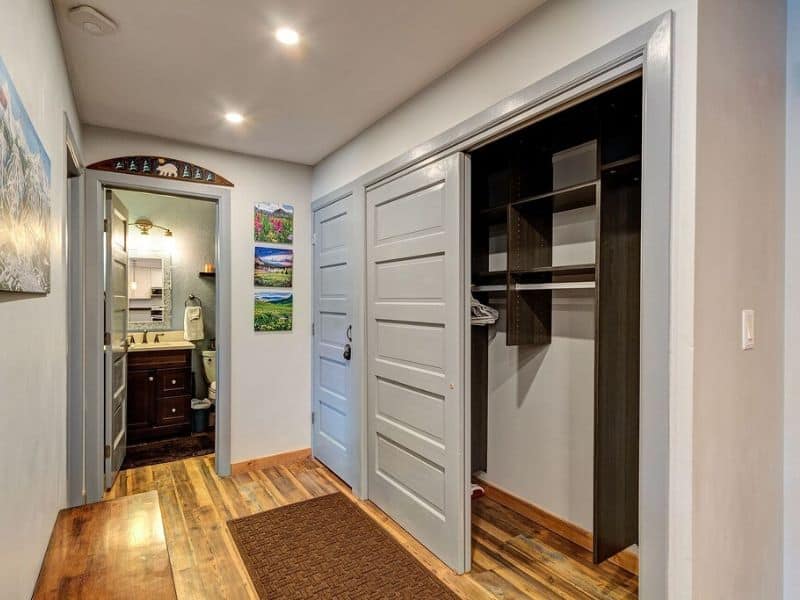 A hallway in a condo with wood floors and a closet.