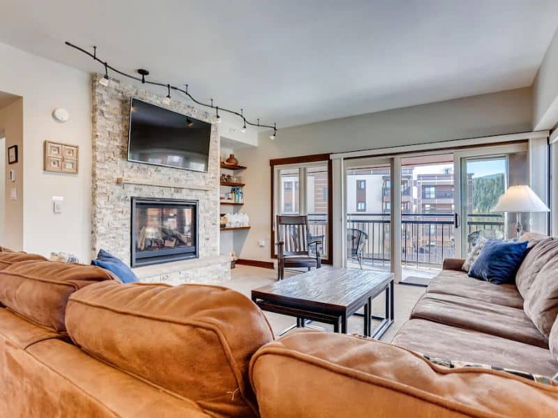 A mountain modern living room in a Breckenridge ski in ski out rental with a stone fireplace and a flat screen tv.