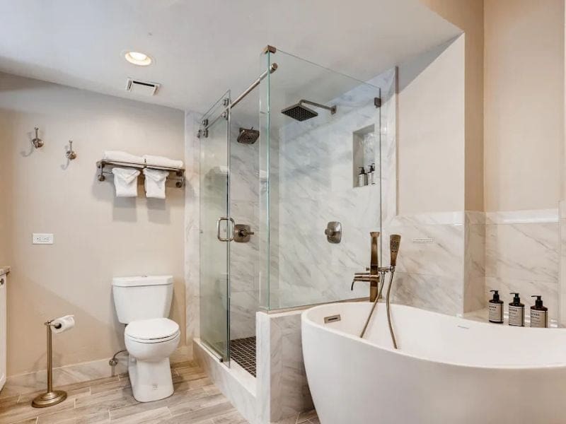 A high-end bathroom in with a tub, toilet and shower with marble tiling.