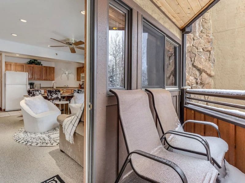A balcony with chairs and a view into an apartment through an open balcony door.