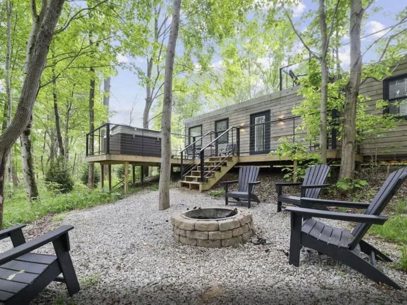 Container cabin in Hocking Hills featuring a fire pit and hot tub and surrounded by woods.
