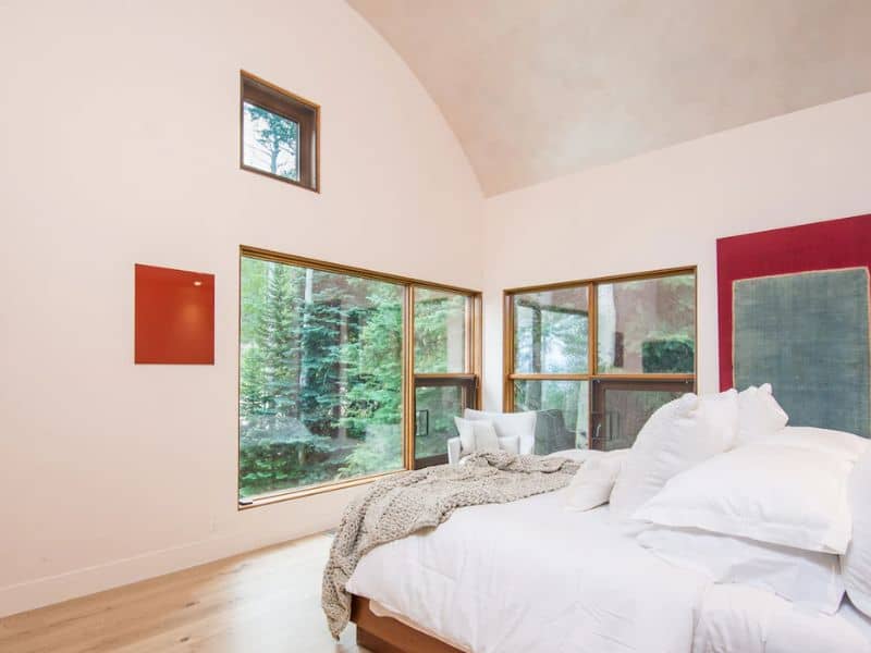 A bedroom with a large bed and a large window with trees outside.