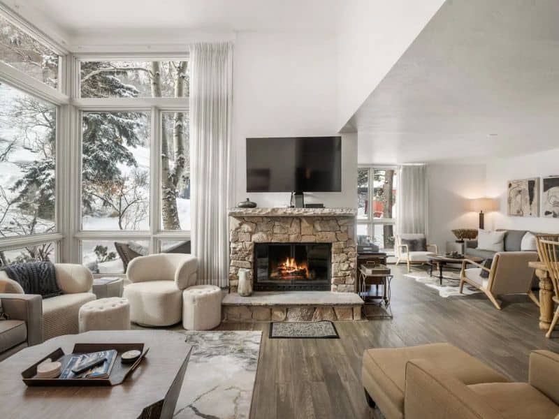 A living room with a fireplace and large windows, located in a ski in ski out condo rental near Shadow Mountain chair lift in Aspen CO.