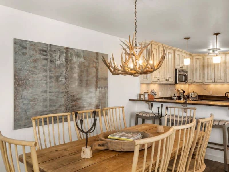 A dining room with a wooden table and chairs and antler chandelier at an Aspen, CO Vrbo.