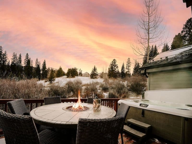A hot tub and fire table on a deck at a ski in ski out Breckenridge rental at sunset.