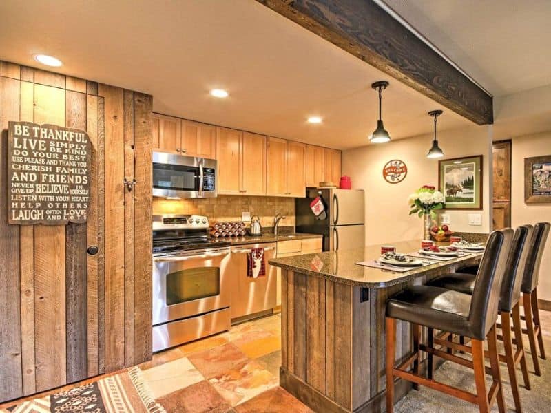 A small kitchen with wood paneling, stainless steel appliances, and bar stools.