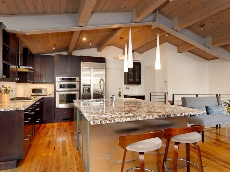 A kitchen with wooden ceilings and a large center island with granite countertops.