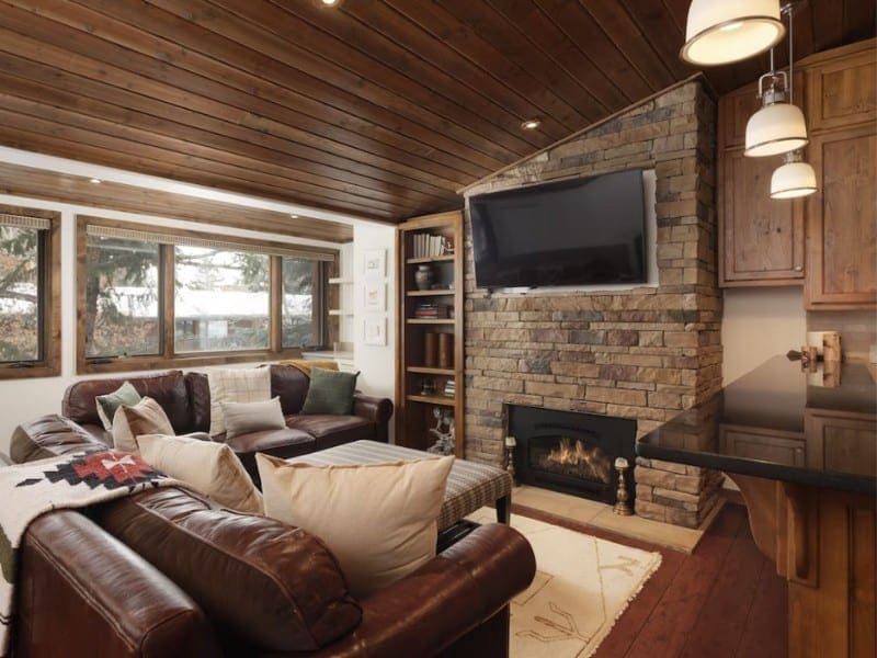 A cozy living room with a stone fireplace, TV, and ski-in ski-out access in Aspen CO.
