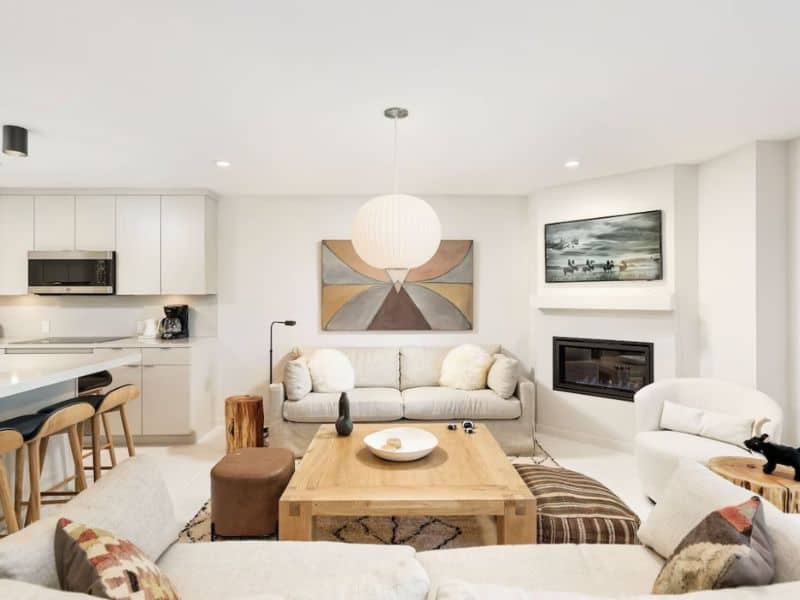 A contemporary living room and kitchen with white furniture in Aspen, CO with ski in ski out access to Snowmass Mountain.