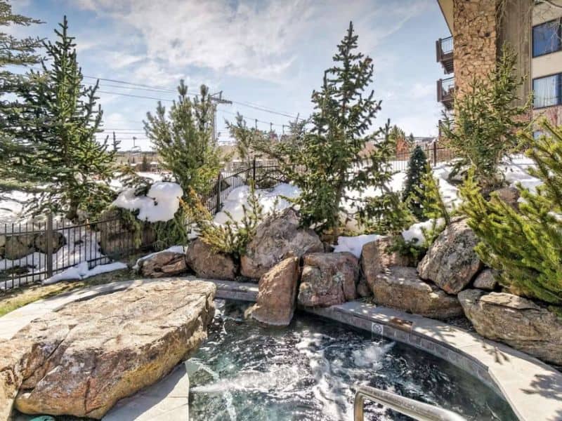 A hot tub surrounded by rocks, snow, and trees in Aspen, CO.