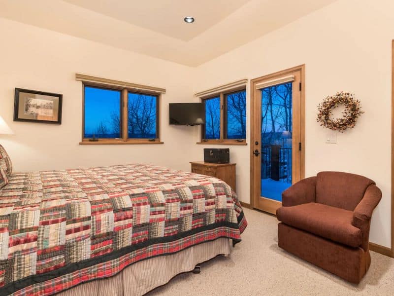 A bedroom with a large bed with a quilted blanket, chair, and TV.