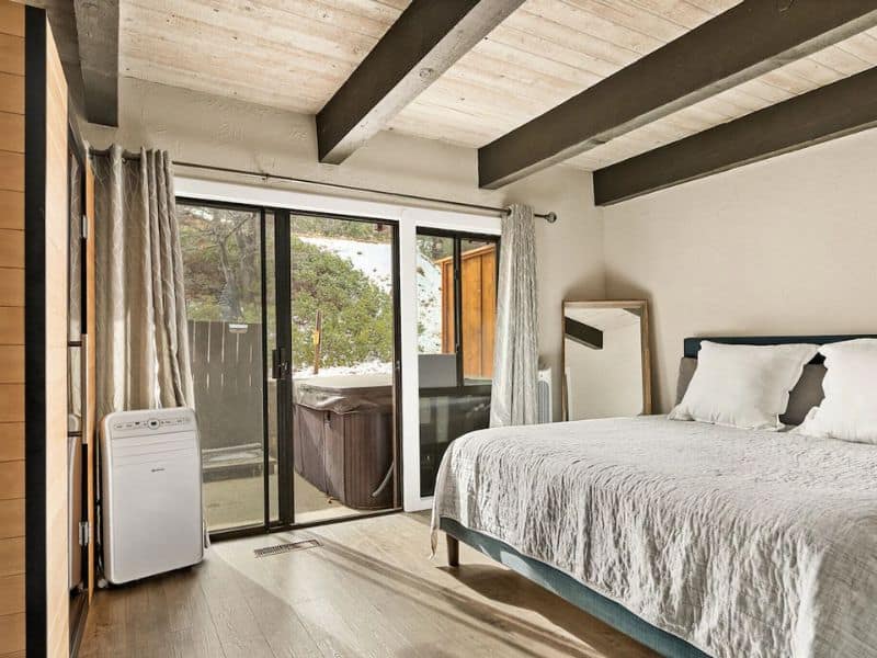 Minimalist bedroom with direct deck access in a cabin, featuring a large bed and a portable air purifier.