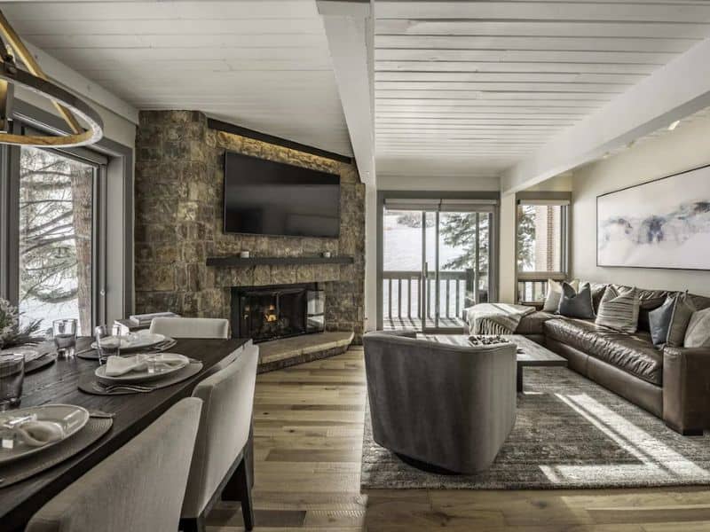 A contemporary living room with a stone fireplace and mountain view at a true ski in ski out condo rental in Aspen CO
