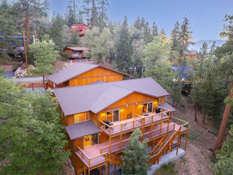 Aerial view of a spacious Big Bear winter cabin surrounded by dense trees, showcasing multiple decks and an inviting design ideal for a cabin rental near Bear Mountain in Big Bear.