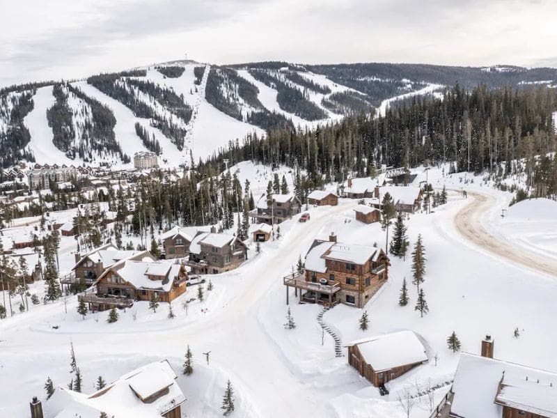 Aerial view showcasing a collection of luxurious ski in ski out rentals in Big Sky, Montana, nestled among snowy slopes and pine trees.